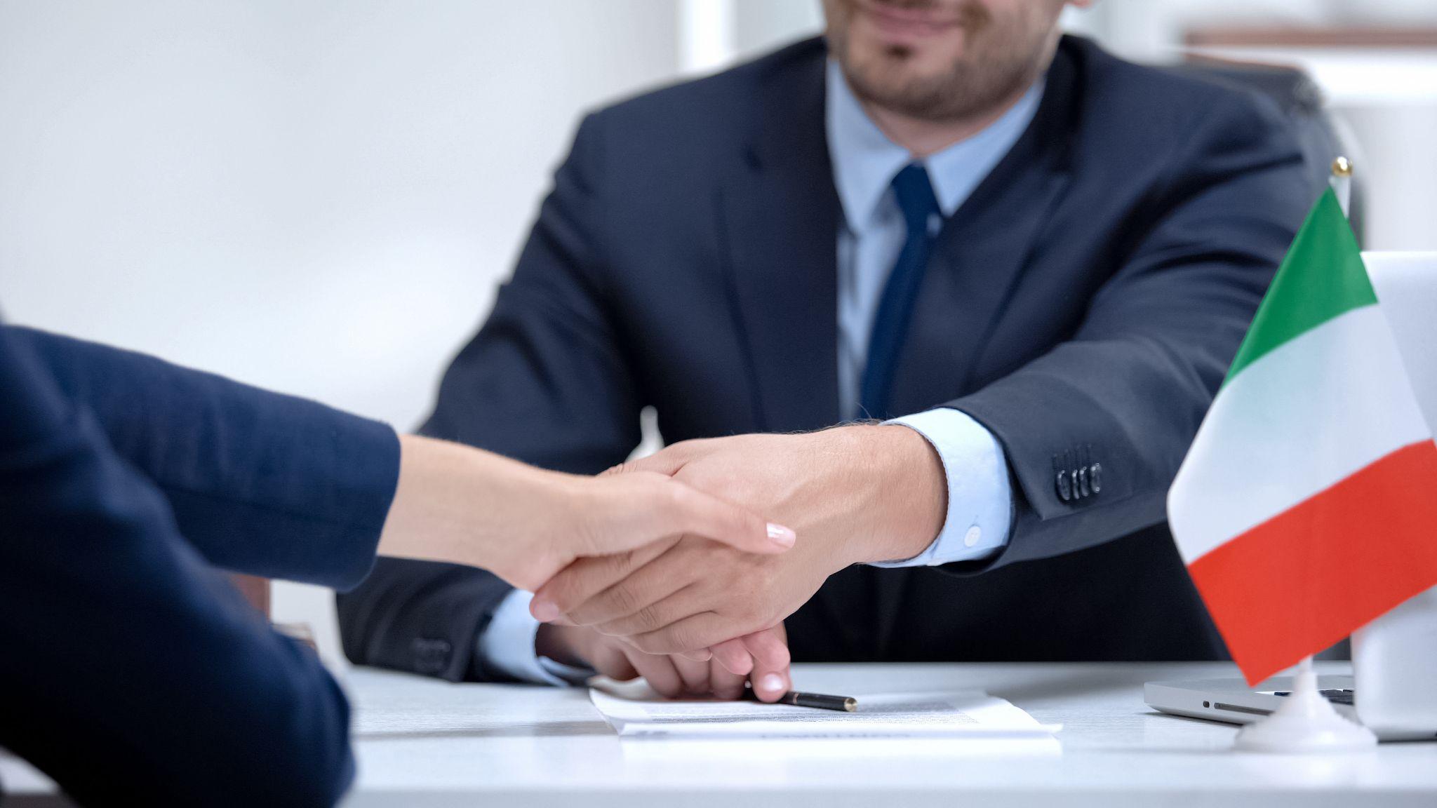 A lawyer with an Italian flag on his desk shaking hands