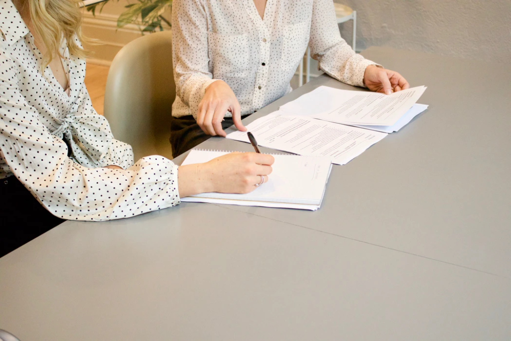 mulher a assinar num papel ao lado de uma mulher prestes a tocar nos documentos