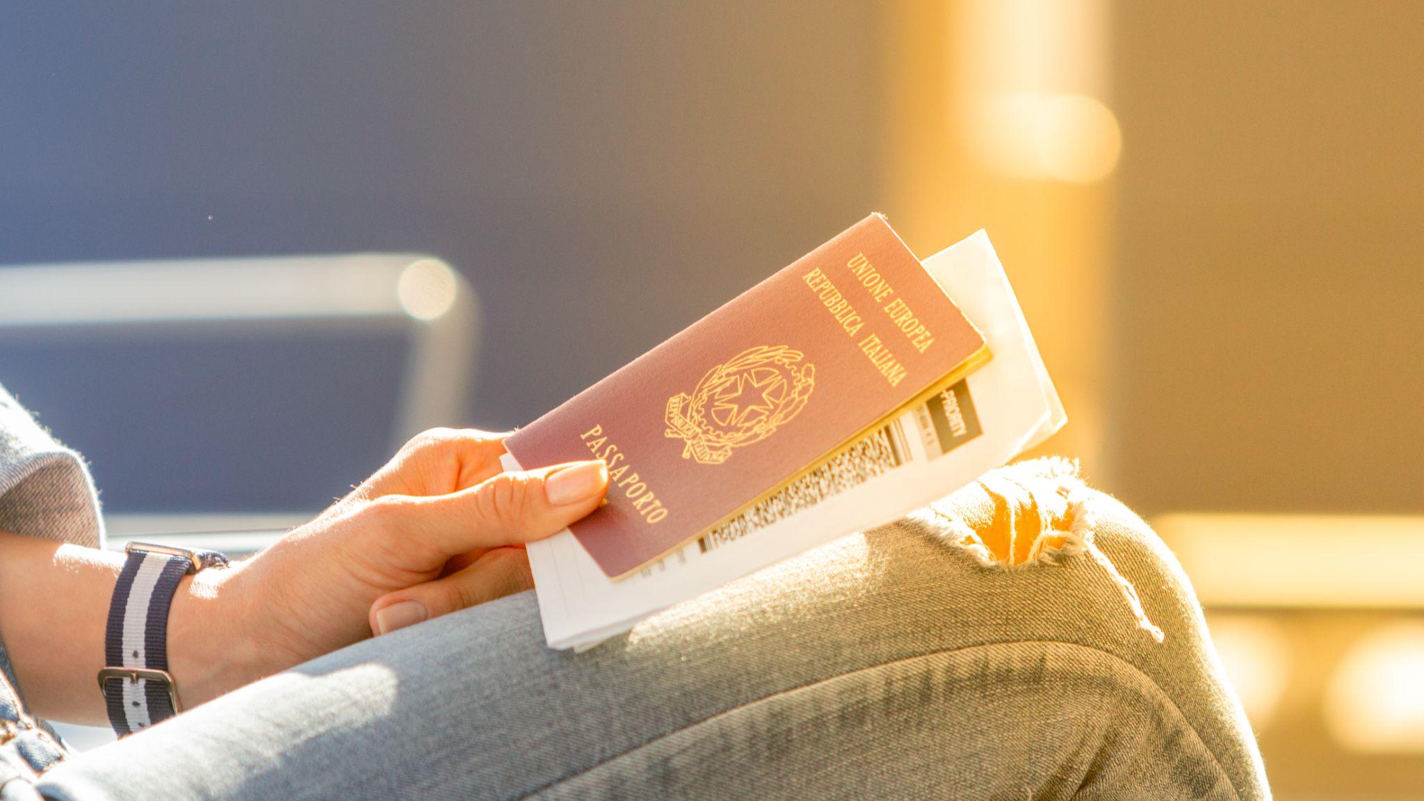 Pasaporte italiano y tarjeta de embarque en manos de una mujer que espera la salida de un vuelo en la sala de espera.