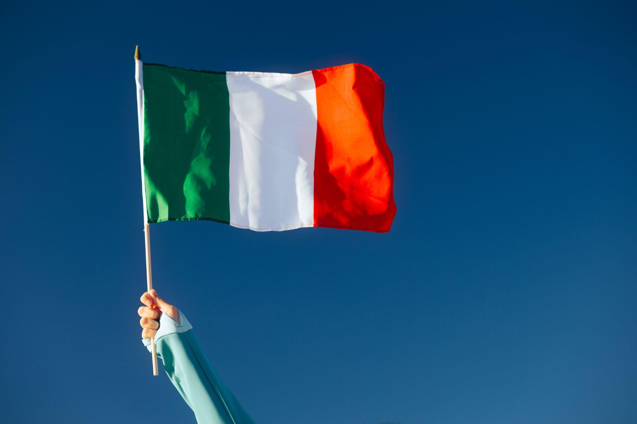The Italian flag being held up in front of a blue sky