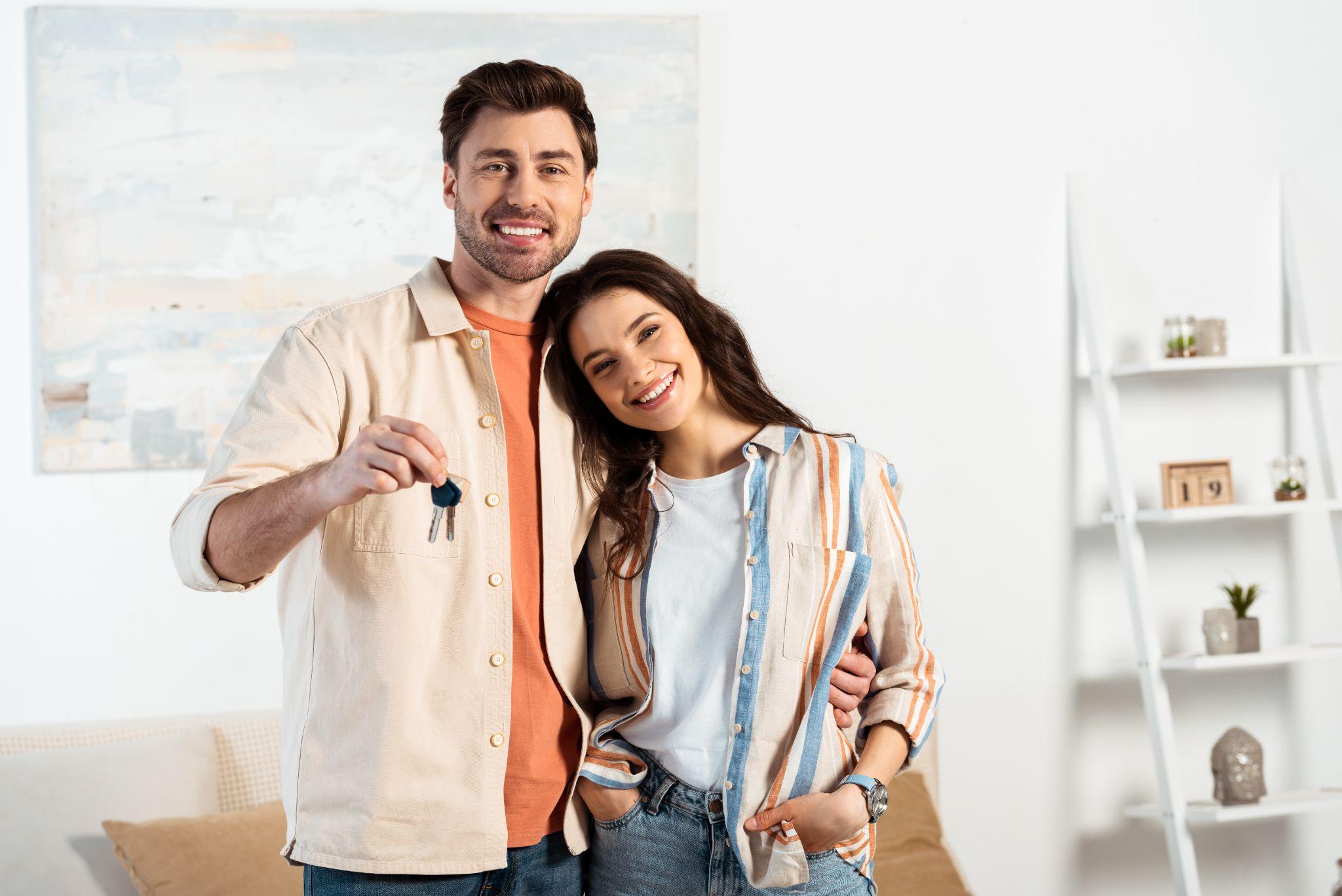 A couple in an apartment holding up their keys smiling