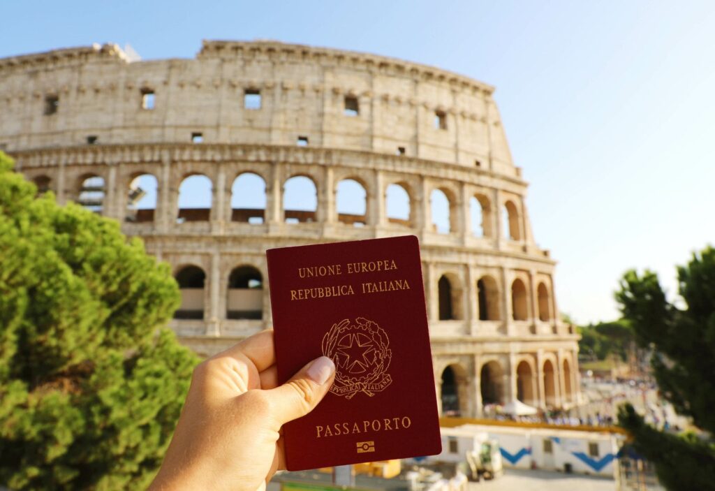 Concepto de ciudadanía: la mano sostiene el pasaporte italiano frente al Coliseo de Roma.