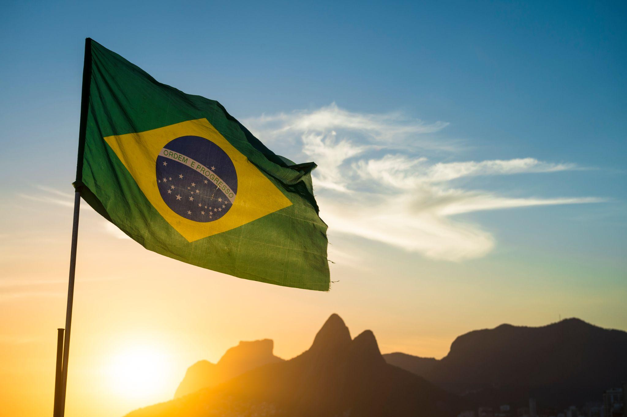 Brazilian flag waving backlit in front of the golden sunset mountain