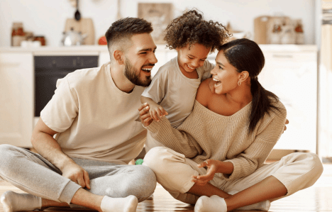 feliz familia multiétnica mamá, papá y niño riendo, jugando y cosquillas en el suelo en la cocina acogedora 