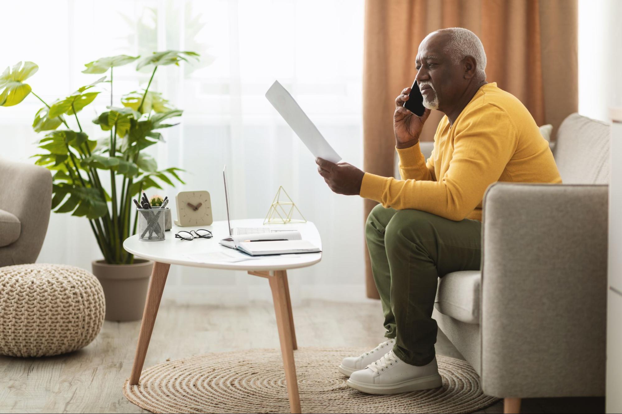 An older man looking at paperwork while talking on the phone