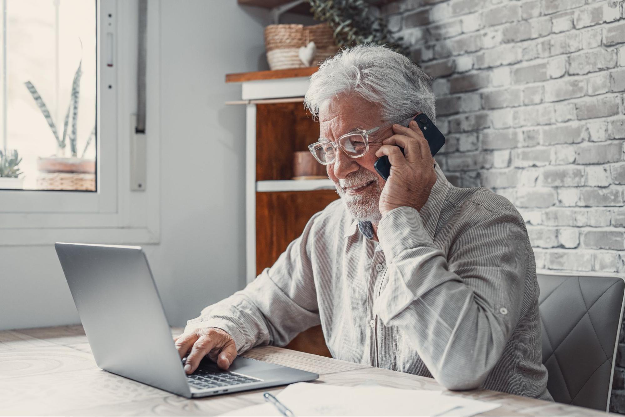 A man talking on the phone while typing on his laptop