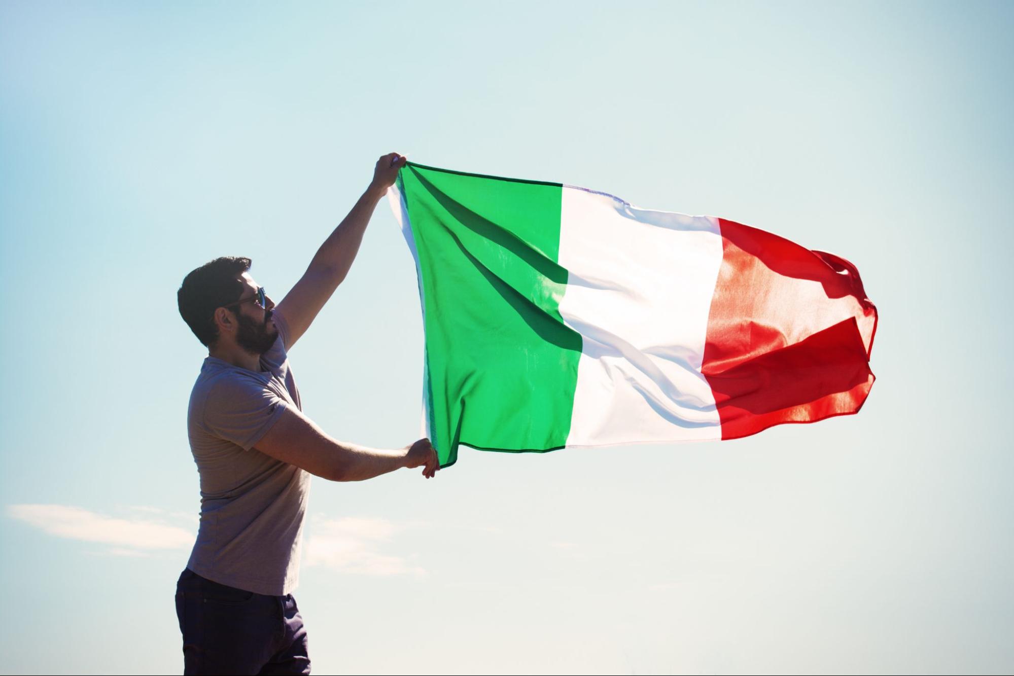Um homem segurando uma bandeira italiana, deixando-a balançar ao vento
